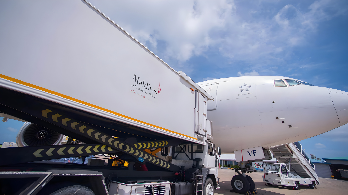 Maldives Inflight Catering truck branded by Montpellier Creative supplying an aircraft on the tarmac under a bright blue sky.