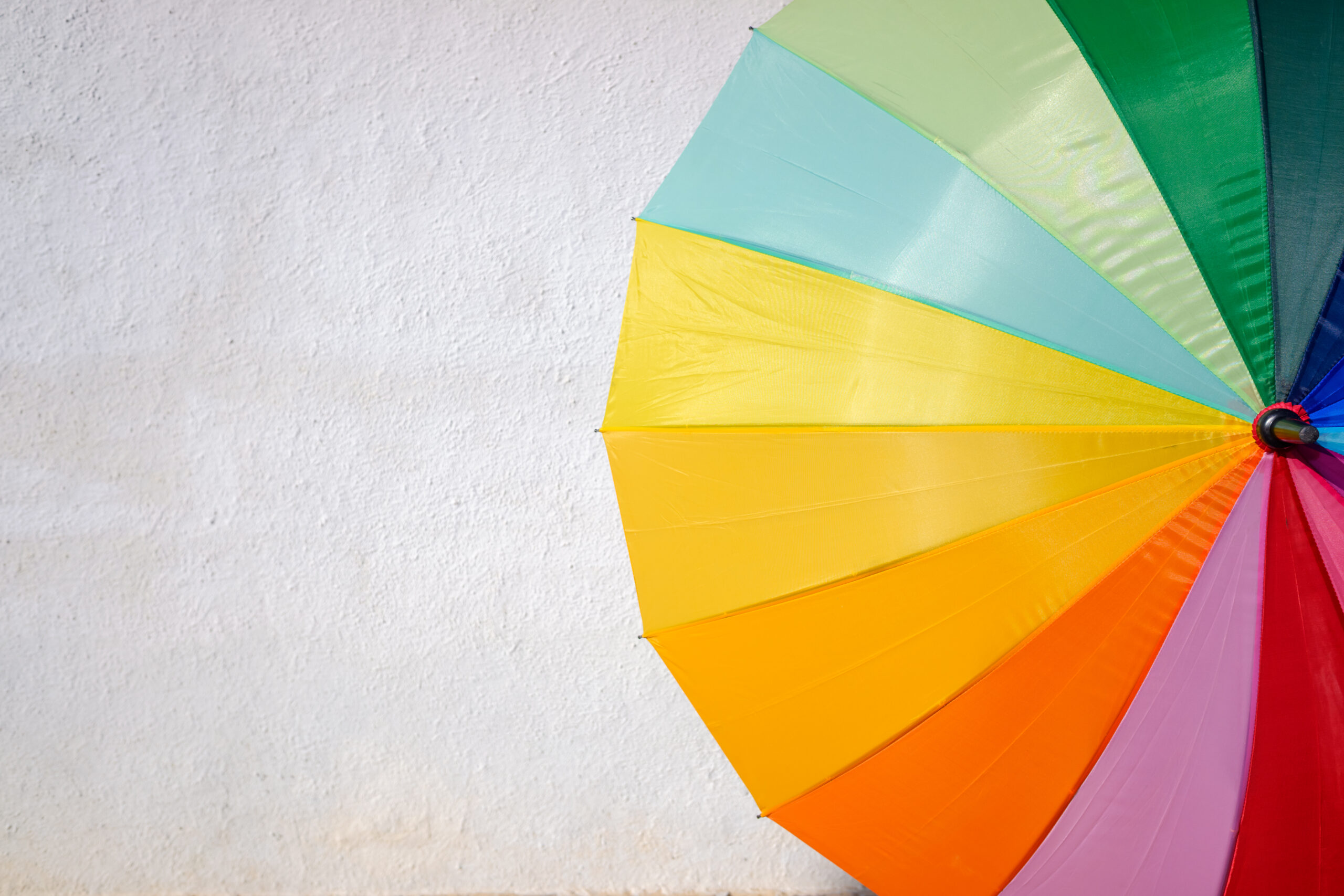 Colourful rainbow umbrella against white wall – visual metaphor for an article exploring the psychology of colour in branding by Montpellier Creative