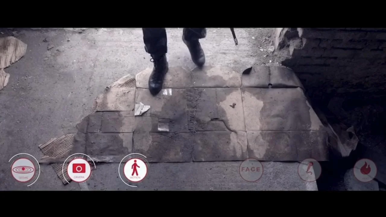 Still from composite video showing tactical boots stepping onto a dusty surface with augmented reality interface overlay, featuring seismic, camera, and motion detection icons – part of a client visual effects project.