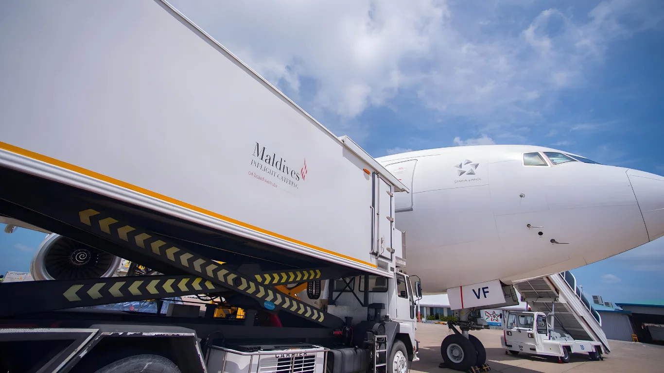 Maldives Inflight Catering truck branded by Montpellier Creative supplying an aircraft on the tarmac under a bright blue sky.