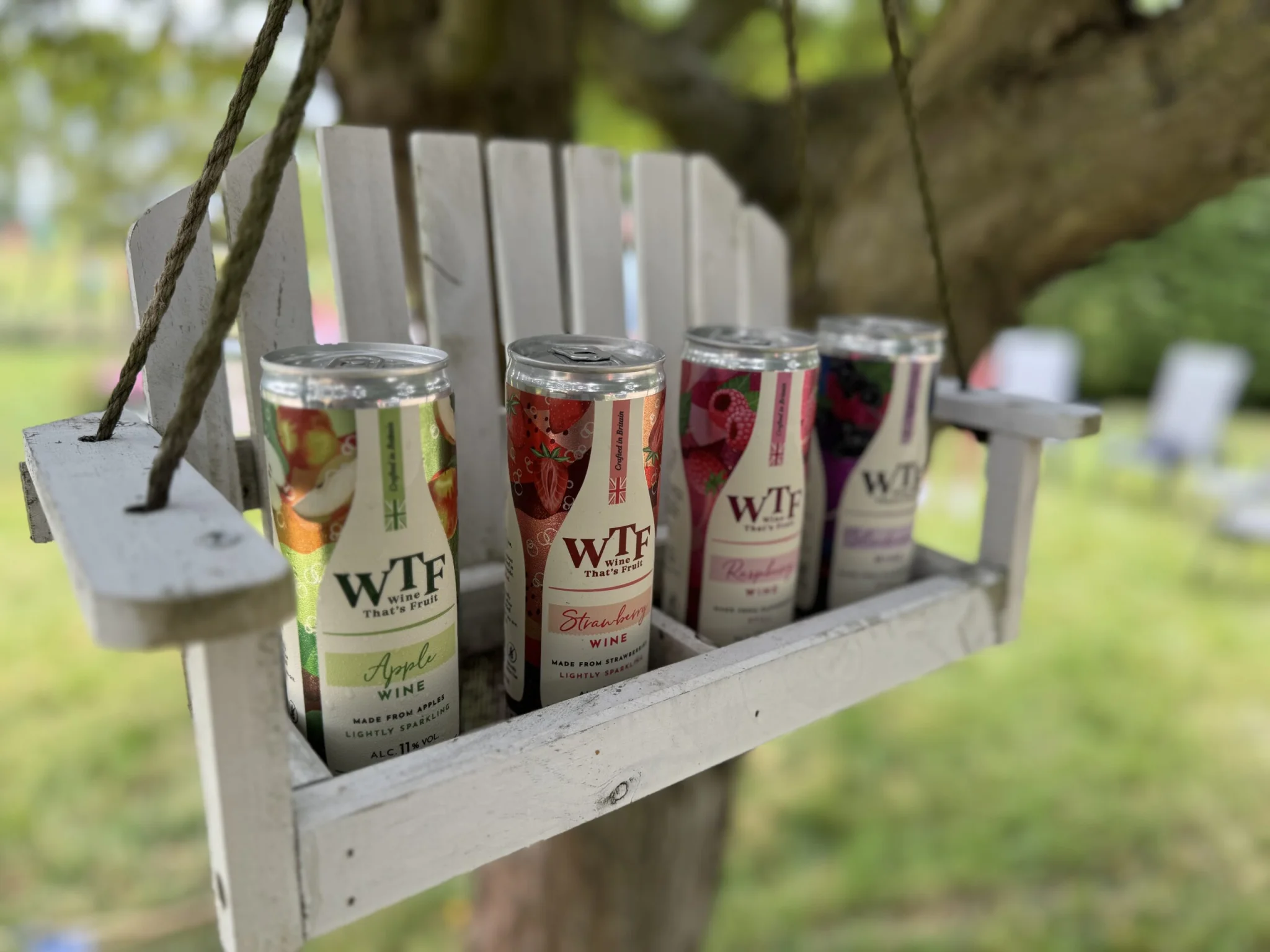 Photo shoot image of WTF canned fruit wines displayed on a rustic white wooden swing, set outdoors in a leafy garden, showcasing vibrant product packaging for a drinks client