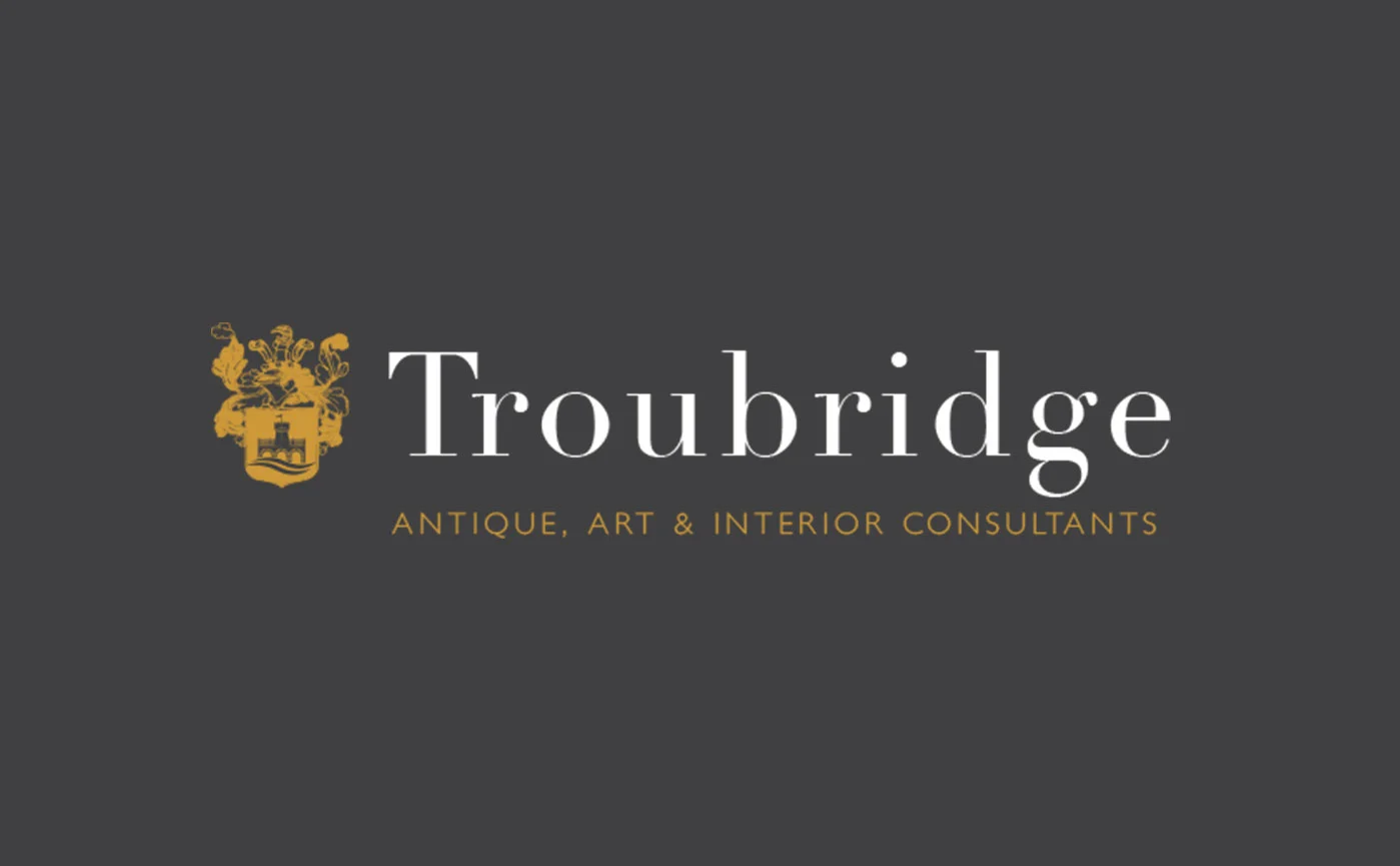 Elegant logo design for Troubridge by Montpellier Creative, featuring a gold crest and serif typography with the tagline ‘Antique, Art & Interior Consultants’ on a dark background.