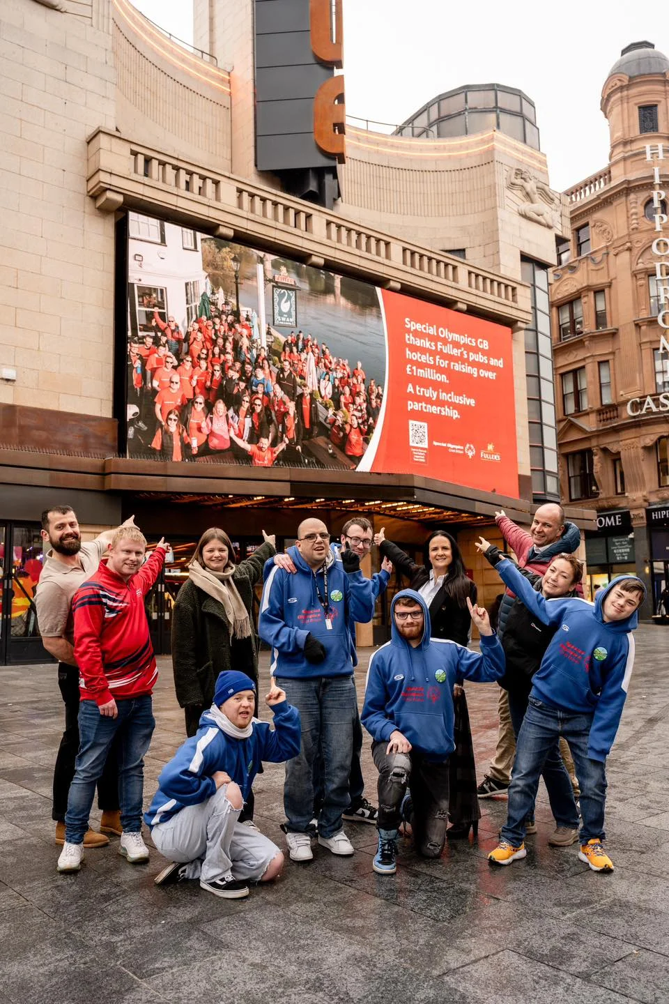 Special Olympics GB athletes and supporters celebrate in front of a giant Leicester Square billboard—designed by Montpellier Creative—thanking Fuller’s pubs and hotels for raising over £1 million, showcasing a truly inclusive partnership.